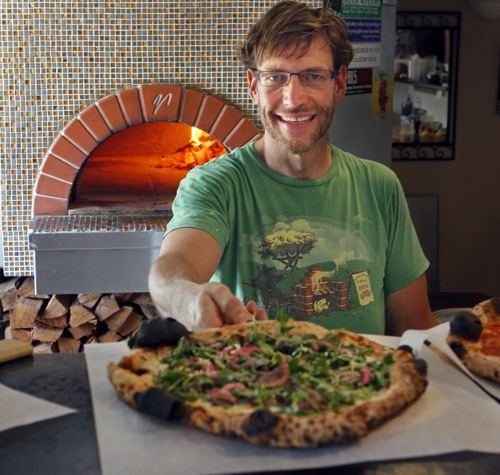 Man serving up a nice, crusty pizza in front of a big wood-fired pizza oven