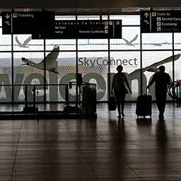 A mostly-empty airport terminal, two travelers roll their luggage in the distant shadows.